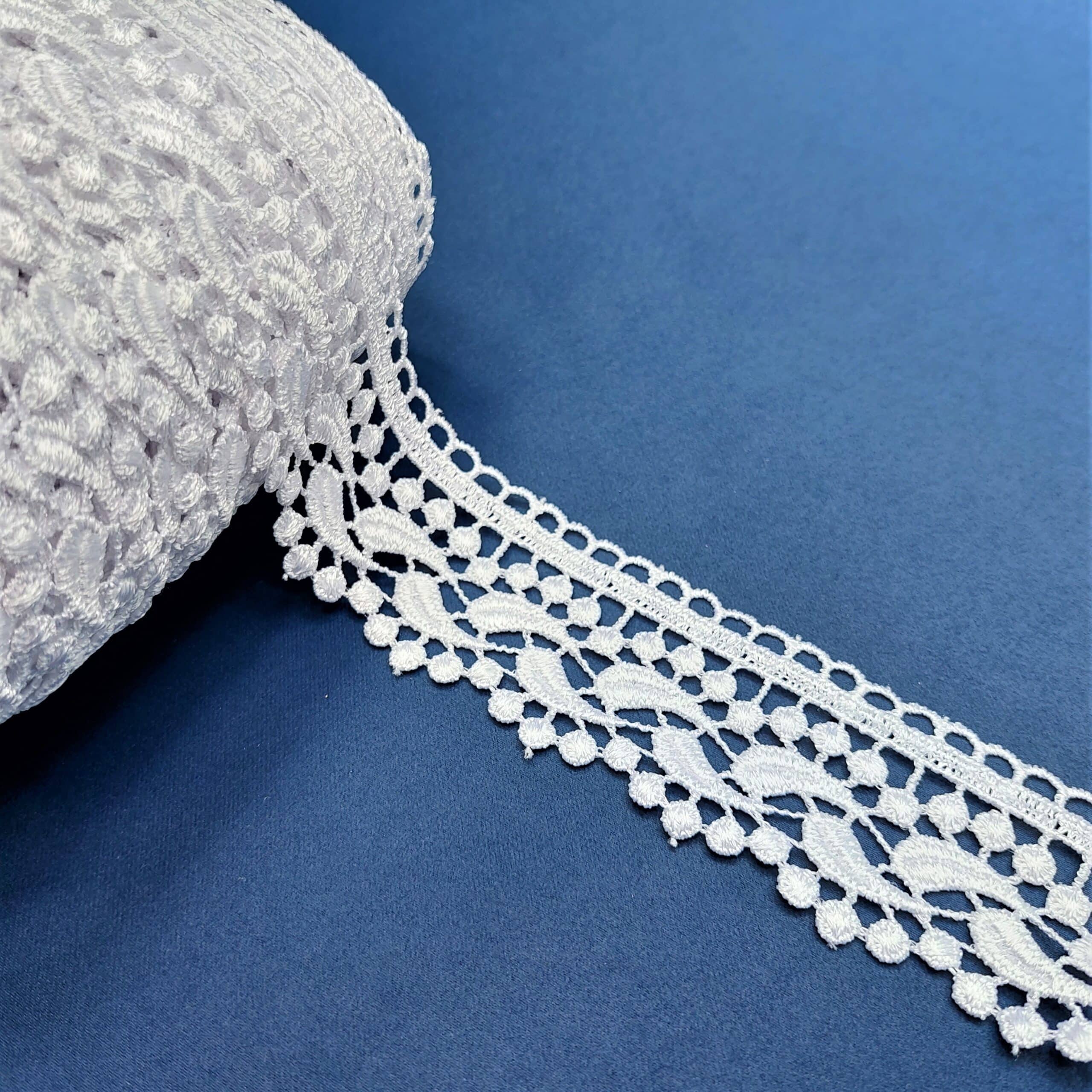 Biała koronka na rolce na niebieskim tle, ozdobna tasiemka do szycia i rękodzieła.