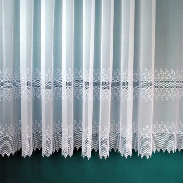 Biała firanka z koronkowym wzorem na tle zielonej ściany, podłoga z jasnego drewna.