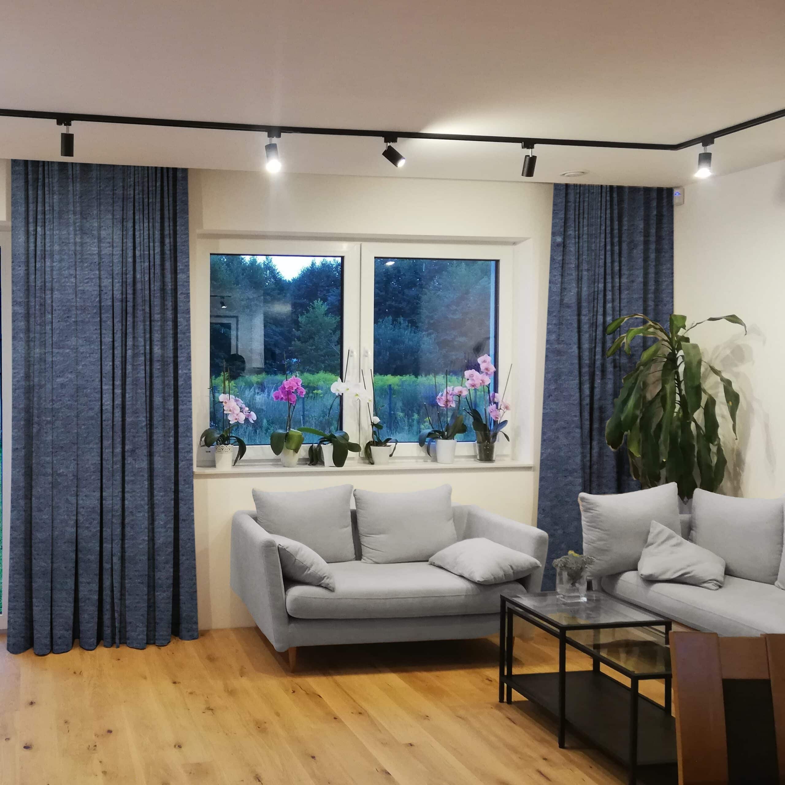 k-realizacja 12665 kw2 Nowoczesny salon z szarymi sofami, drewnianą podłogą i kwiatami na parapecie w oknie, widok na ogród.