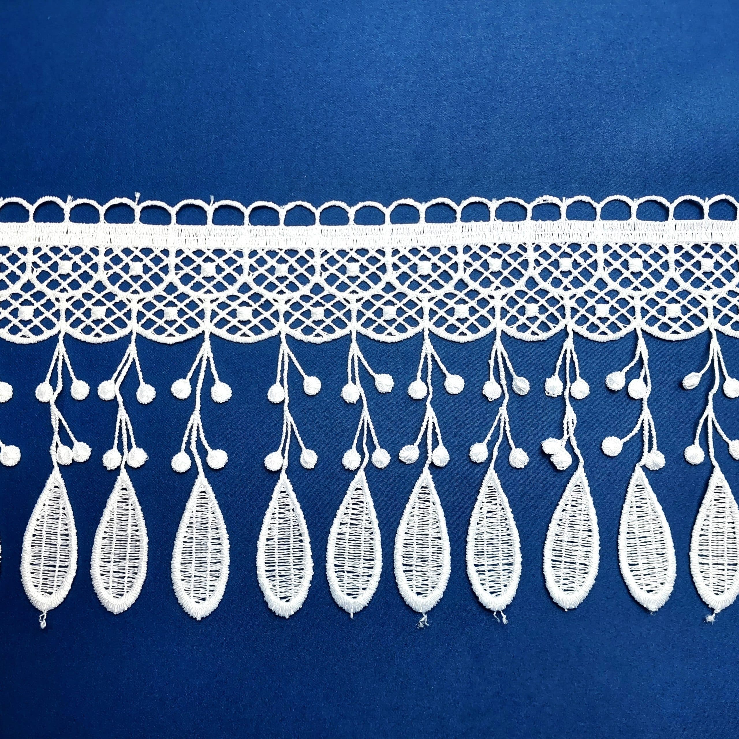 Biały koronkowy wzór na niebieskim tle, z ozdobnymi liśćmi i kropkami, elegancki dodatek do tkanin.