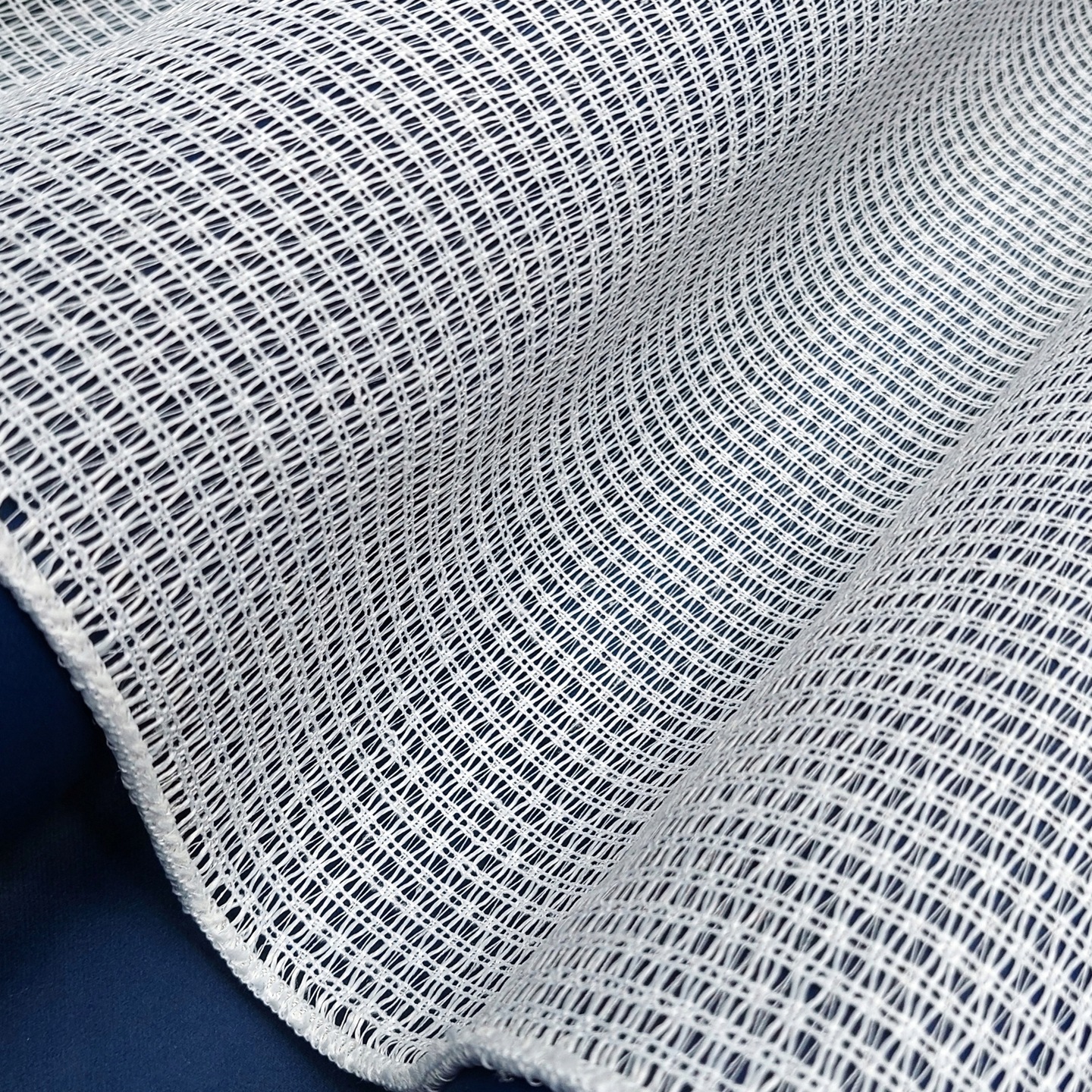 Biała, elastyczna tkanina o drobnym wzorze, idealna na lekkie zasłony lub dekoracje wnętrz.