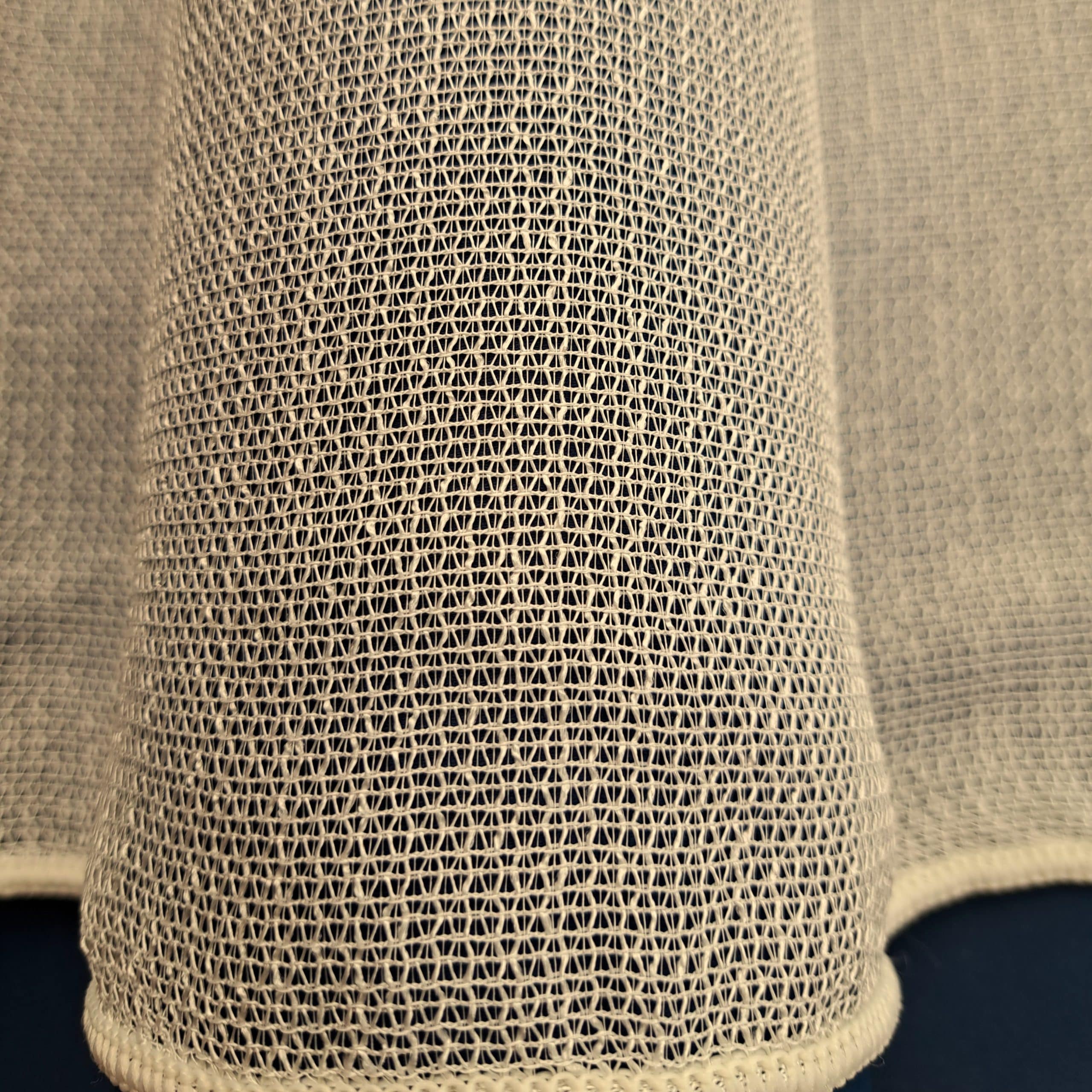 Zbliżenie na fakturę jasnej siatki materiałowej, pokrywającej tkaninę w kształcie falistym.