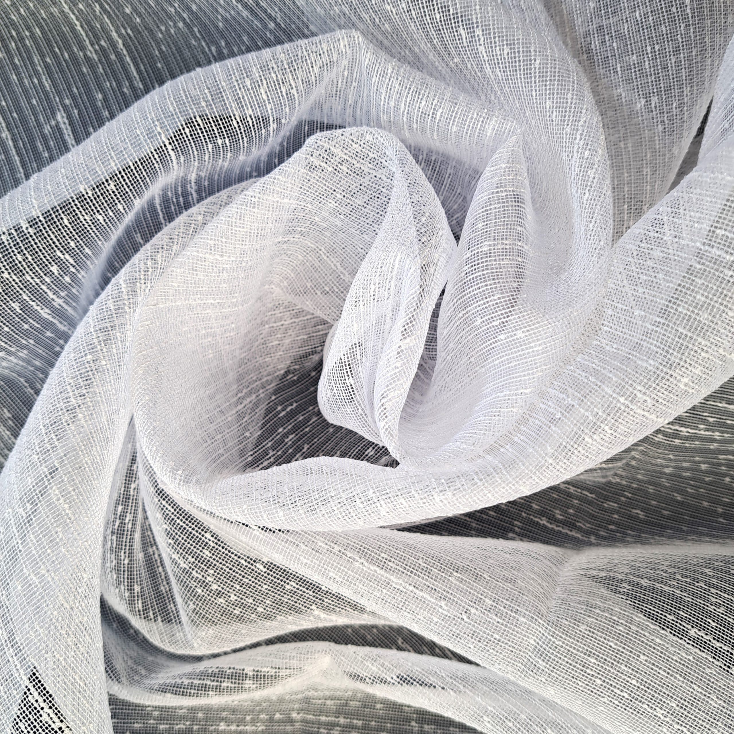 Delikatna biała tkanina typu gaza, sfałdowana w artystyczne wzory, zbliżenie na teksturę materiału.