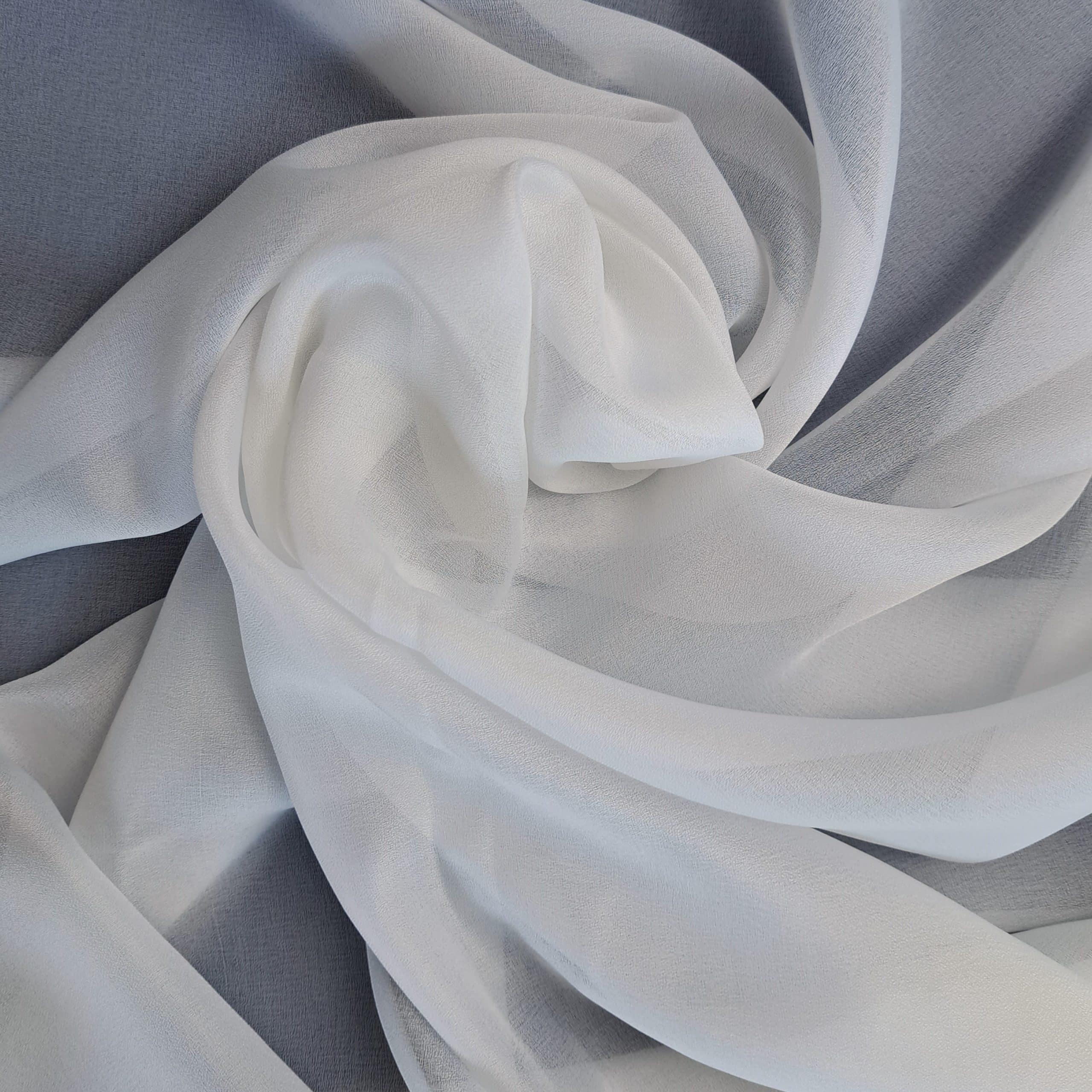 Biała tkanina z organzy ułożona falisto na szarej powierzchni, tworząca elegancki wzór.