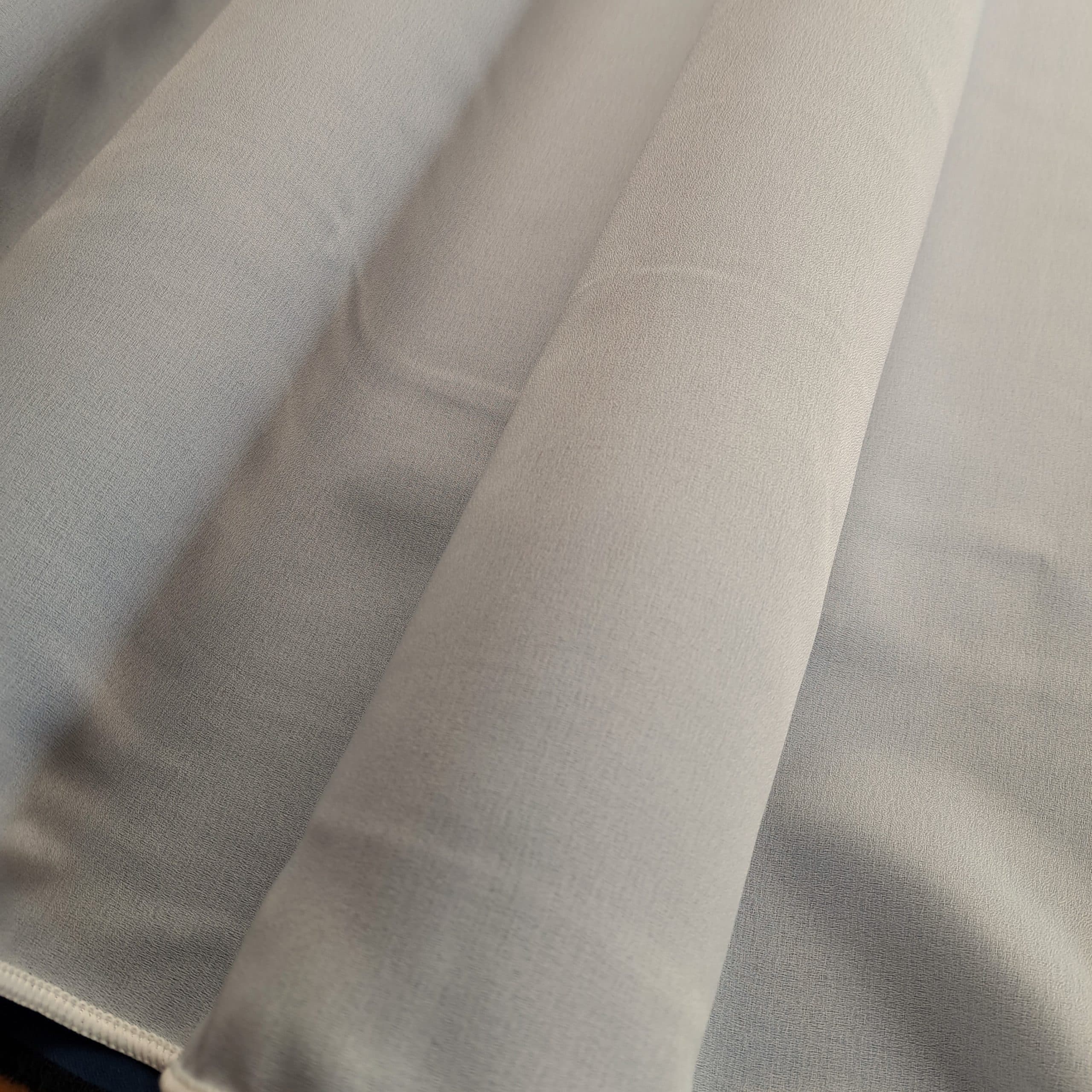 Szary materiał zasłonowy w zbliżeniu, ukazujący fakturę i falowanie tkaniny. Idealne do dekoracji wnętrz.