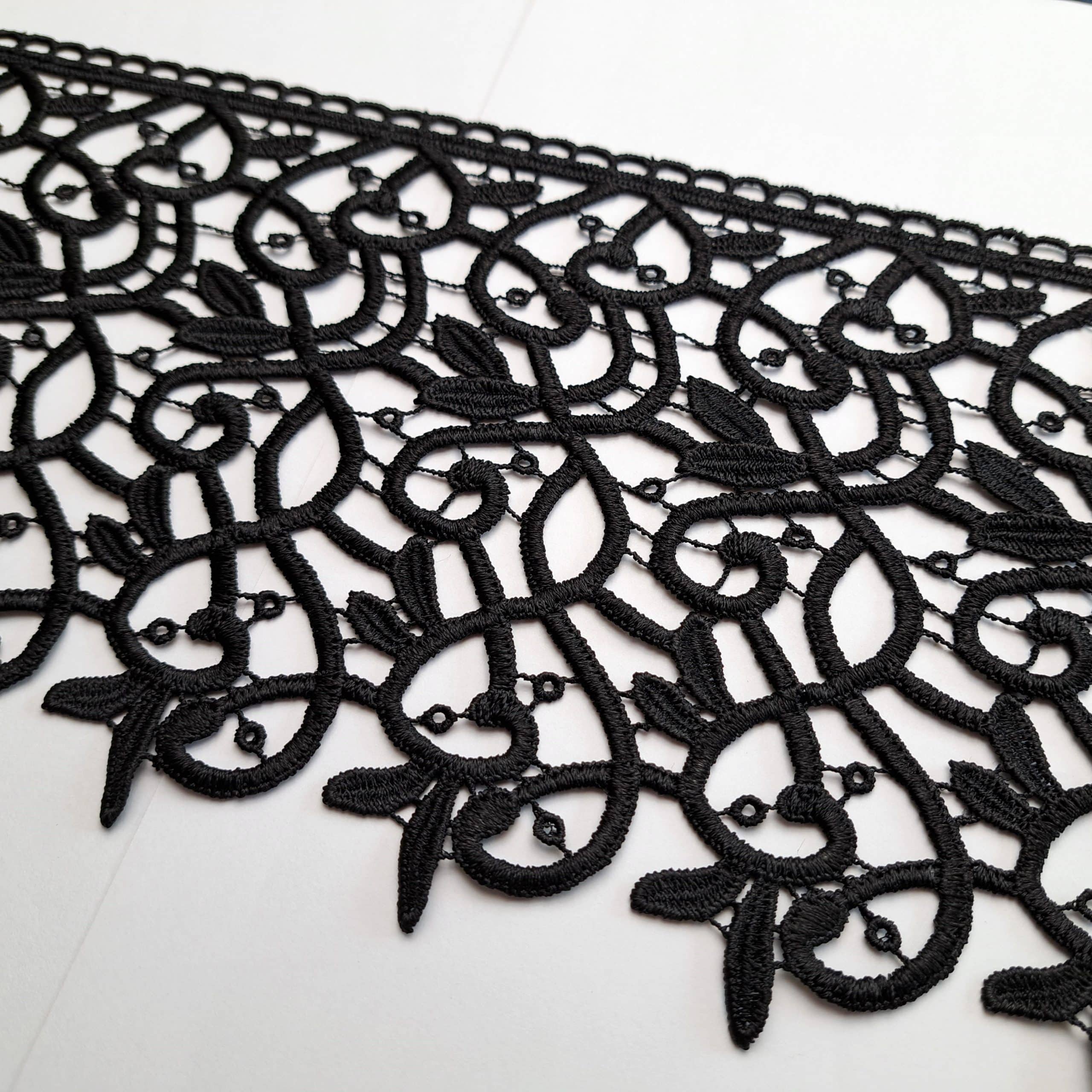 Czarna koronka złożona z ozdobnych, symetrycznych wzorów na białym tle, idealna do eleganckich projektów krawieckich.