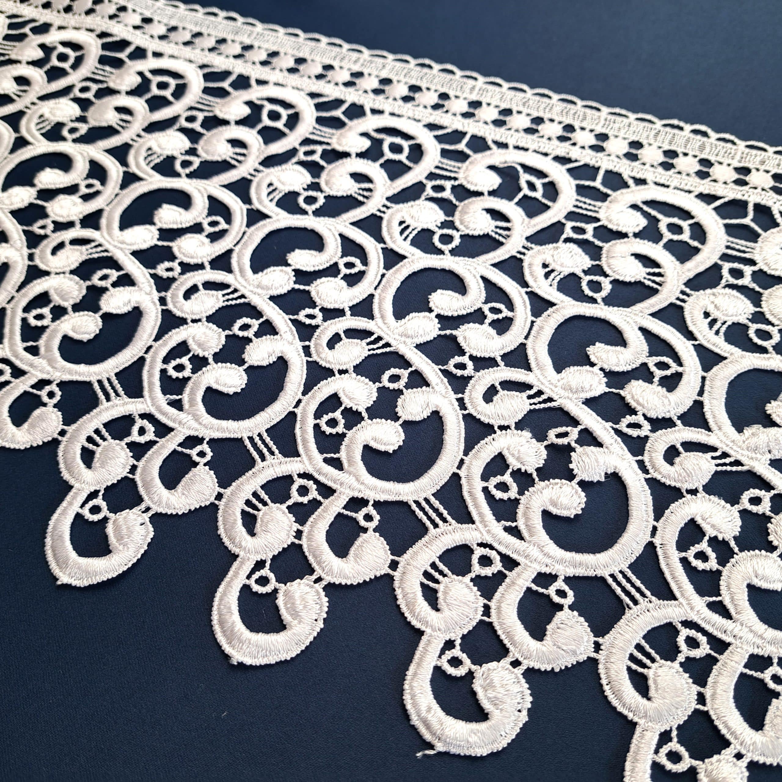 2521-20 3 Biała koronka o złożonym wzorze na granatowym tle, prezentująca elegancki design.