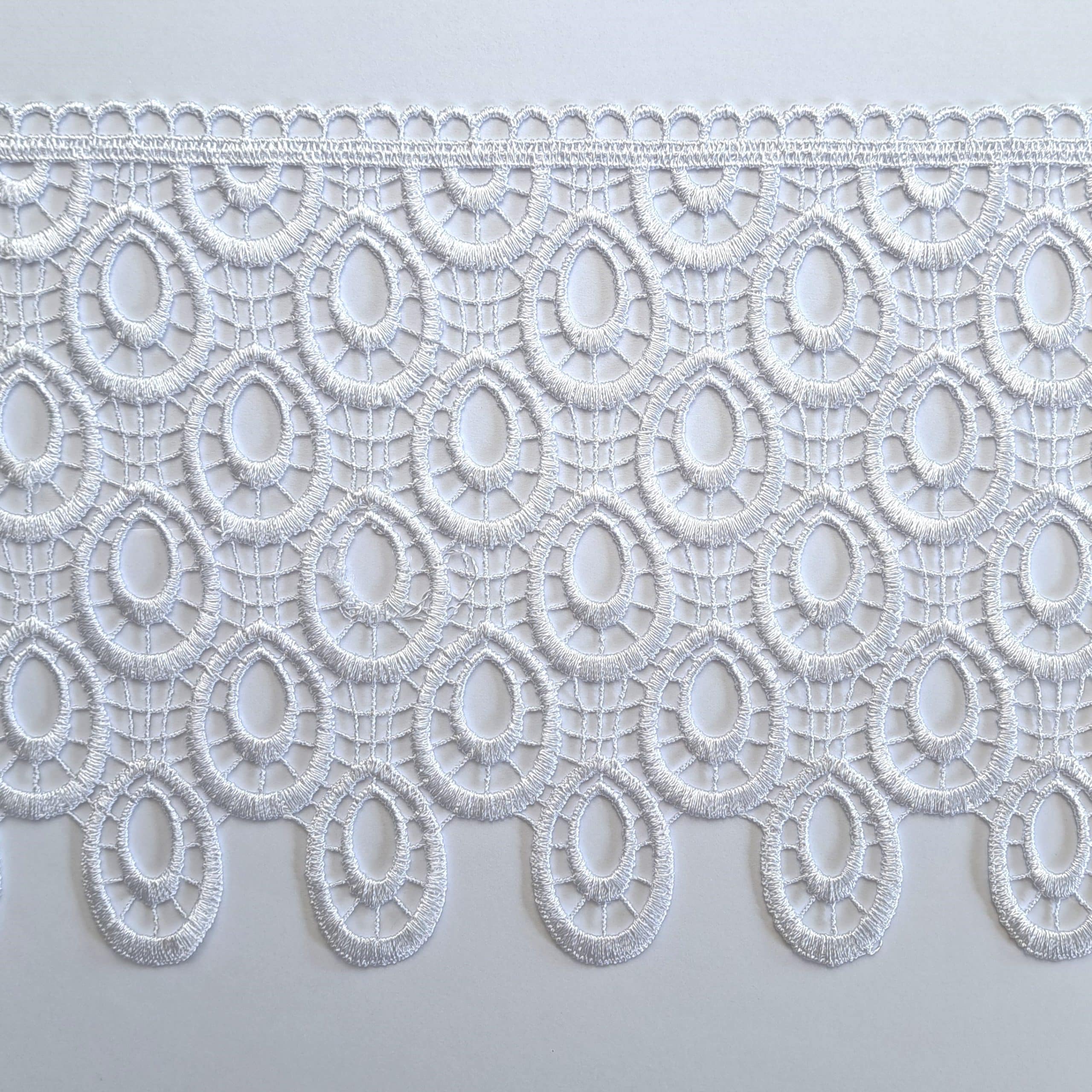 Koronkowa biała tkanina z owalnym wzorem na jasnym tle, delikatny materiał do dekoracji i mody.