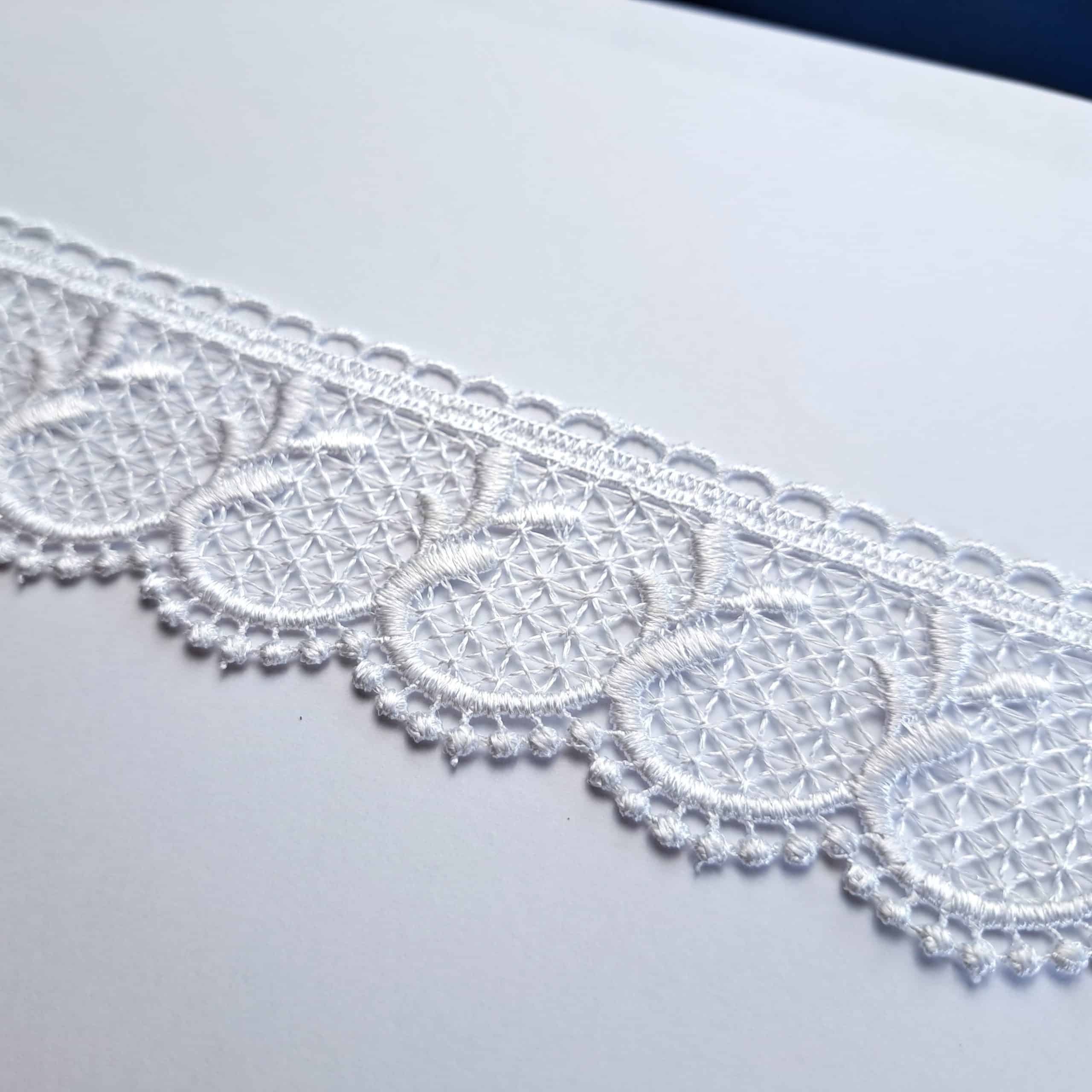 Biała koronkowa taśma na białym tle, delikatny ażurowy wzór owalnych kształtów, idealny do dekoracji tkanin.