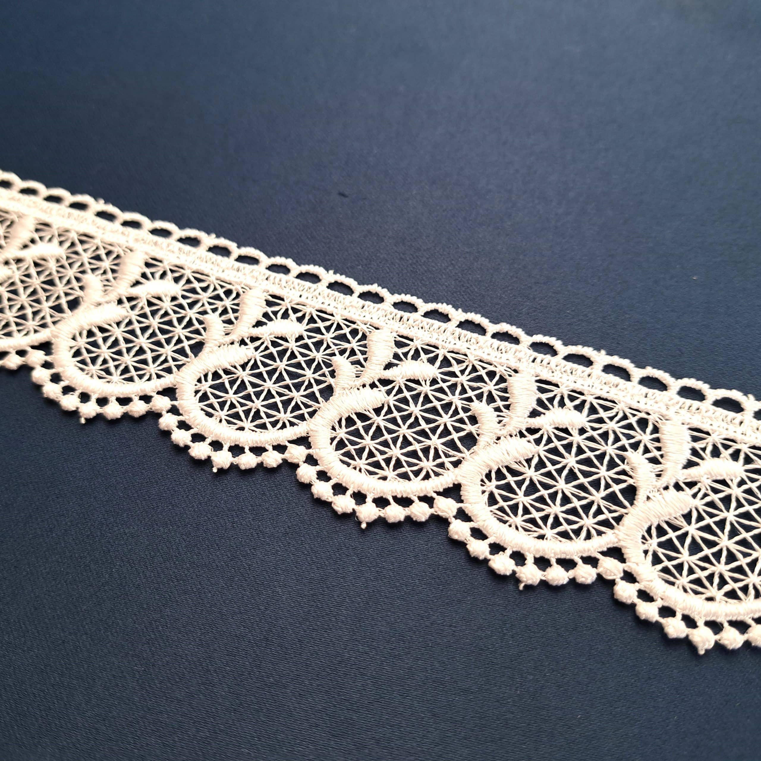 Koronka beżowa złożona z okrągłych wzorów na ciemnym tle.