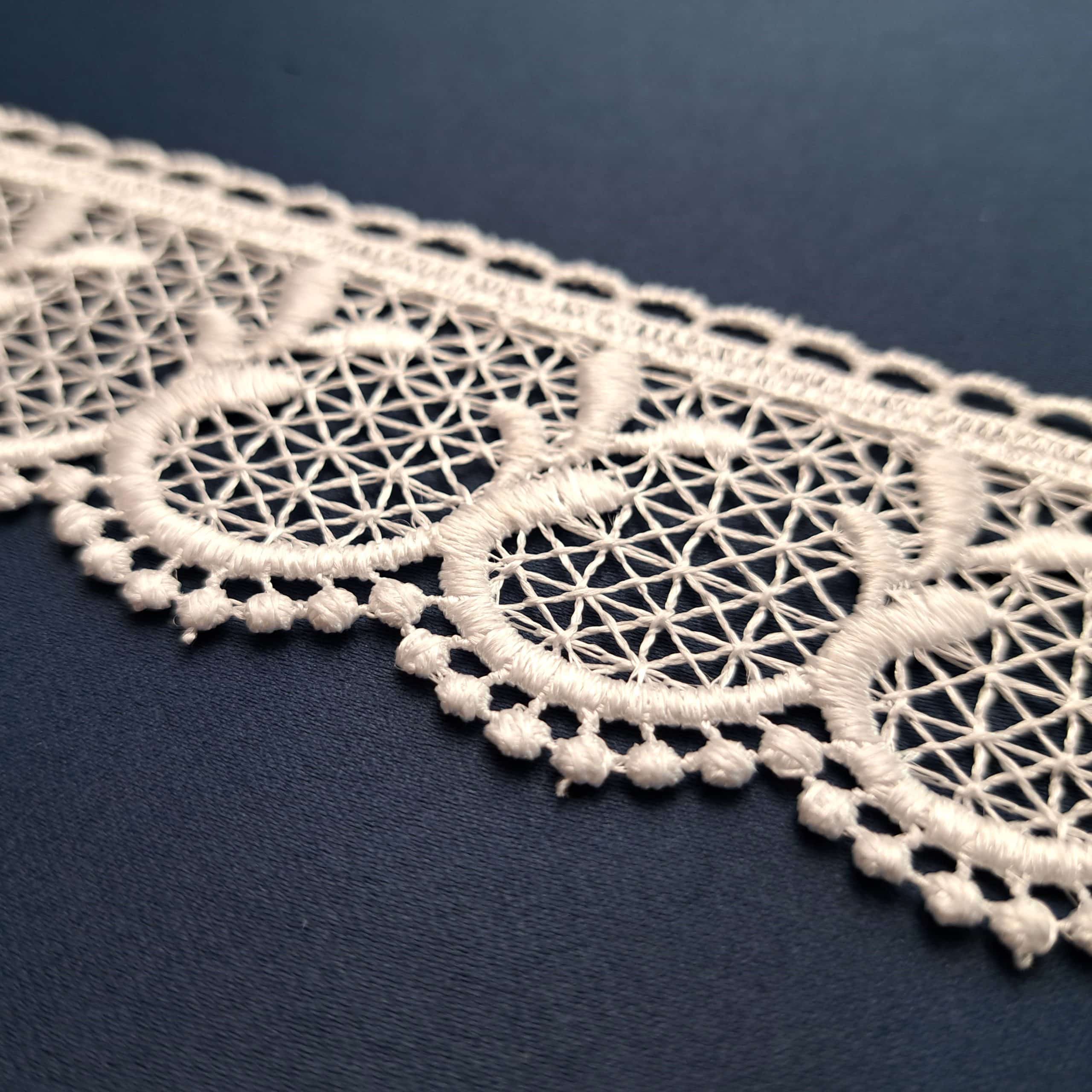 Koronkowa taśma w kolorze białym na ciemnym tle, ozdobiona delikatnym wzorem geometrycznym.