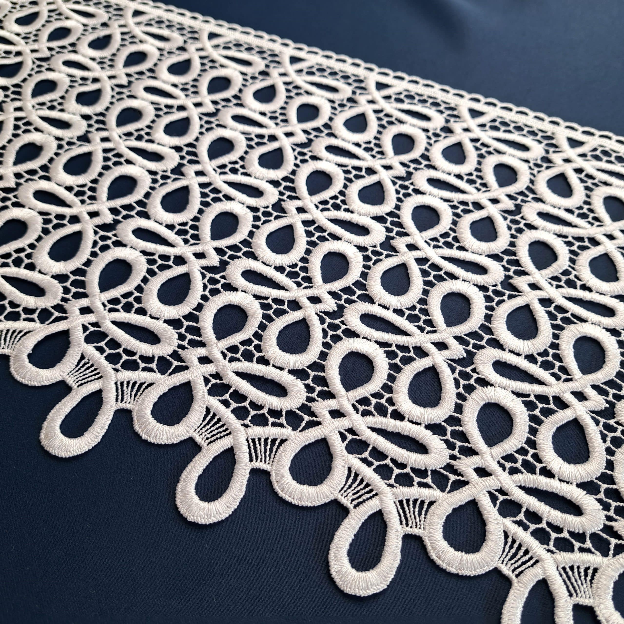 Biała koronka na granatowym tle, misterny wzór z geometrycznymi kształtami; elegancki design do dekoracji.