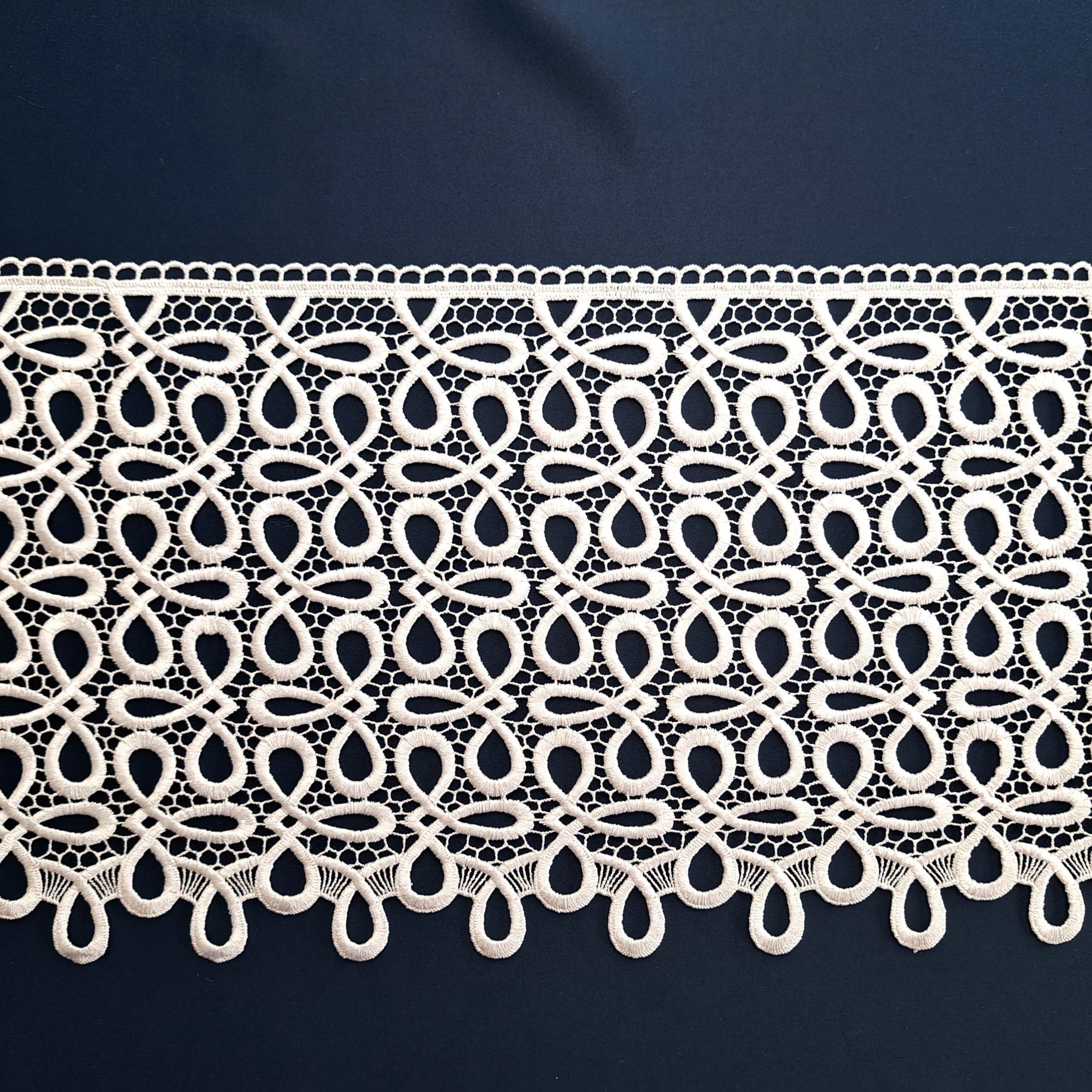 Koronkowa wstęga o delikatnym wzorze na ciemnym tle.