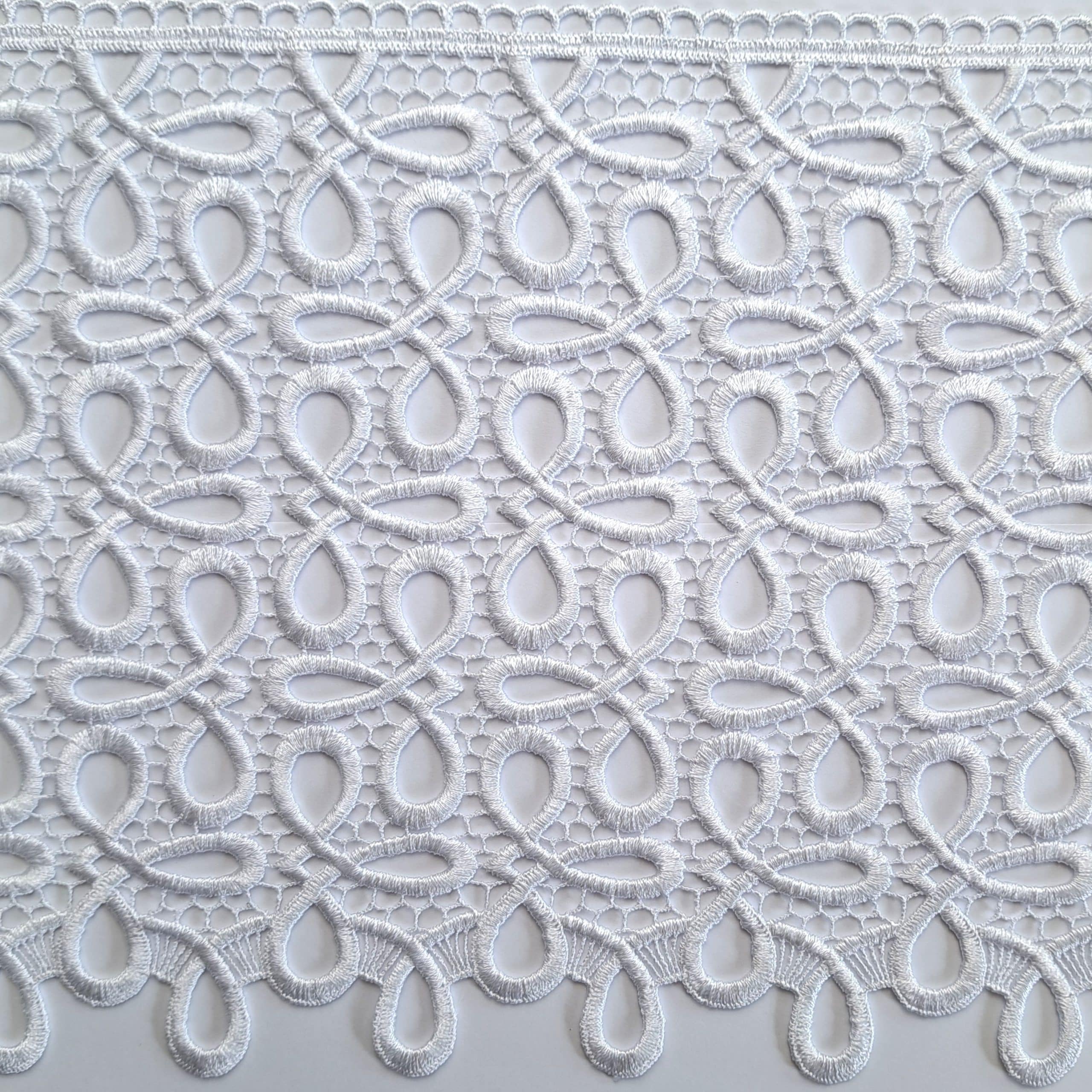 Biała koronkowa tkanina z delikatnym wzorem w pętle i krople, elegancka dekoracja.