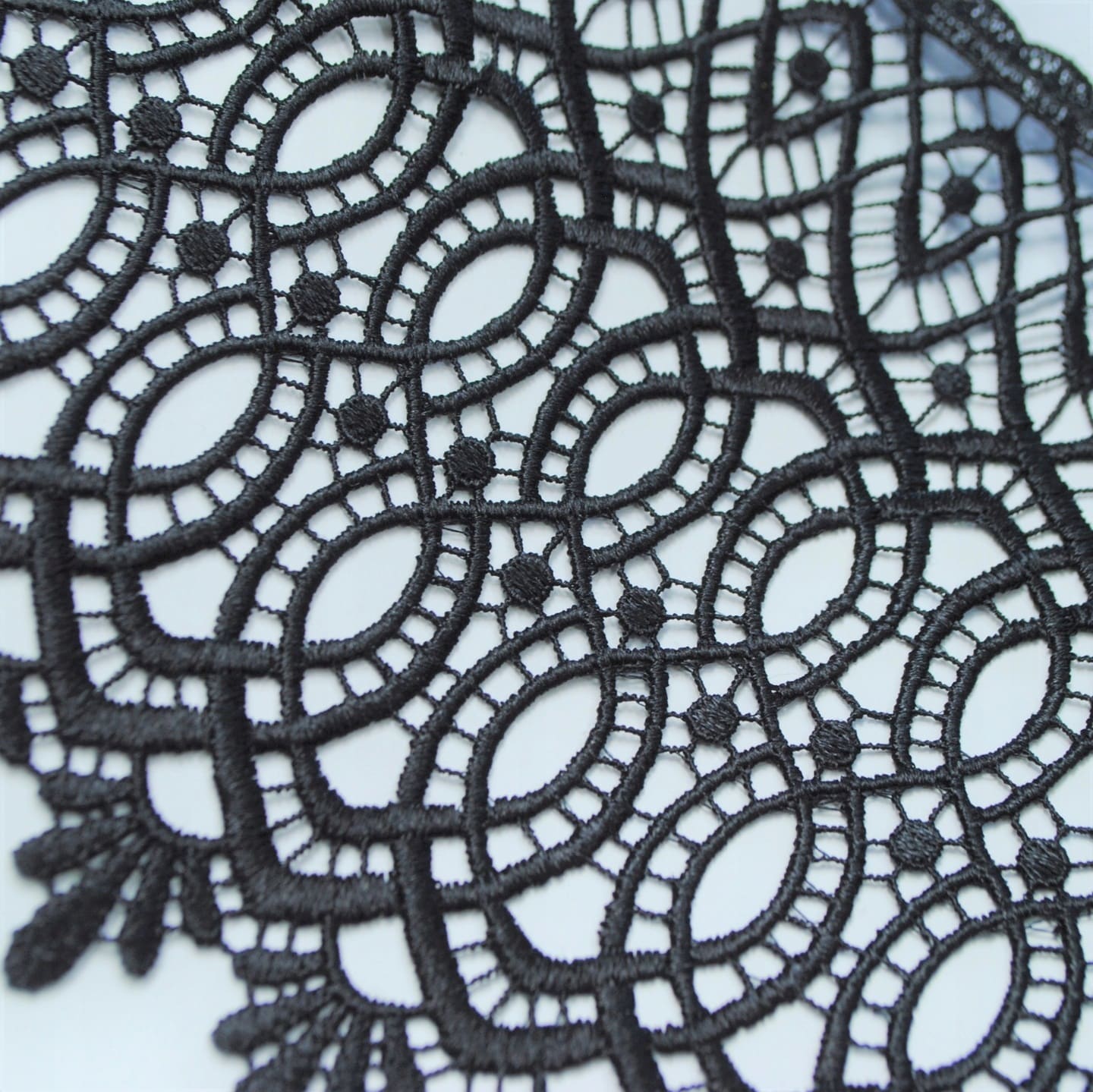 Czarna koronka o skomplikowanym wzorze geometrycznym, elegancka tekstura tkaniny.