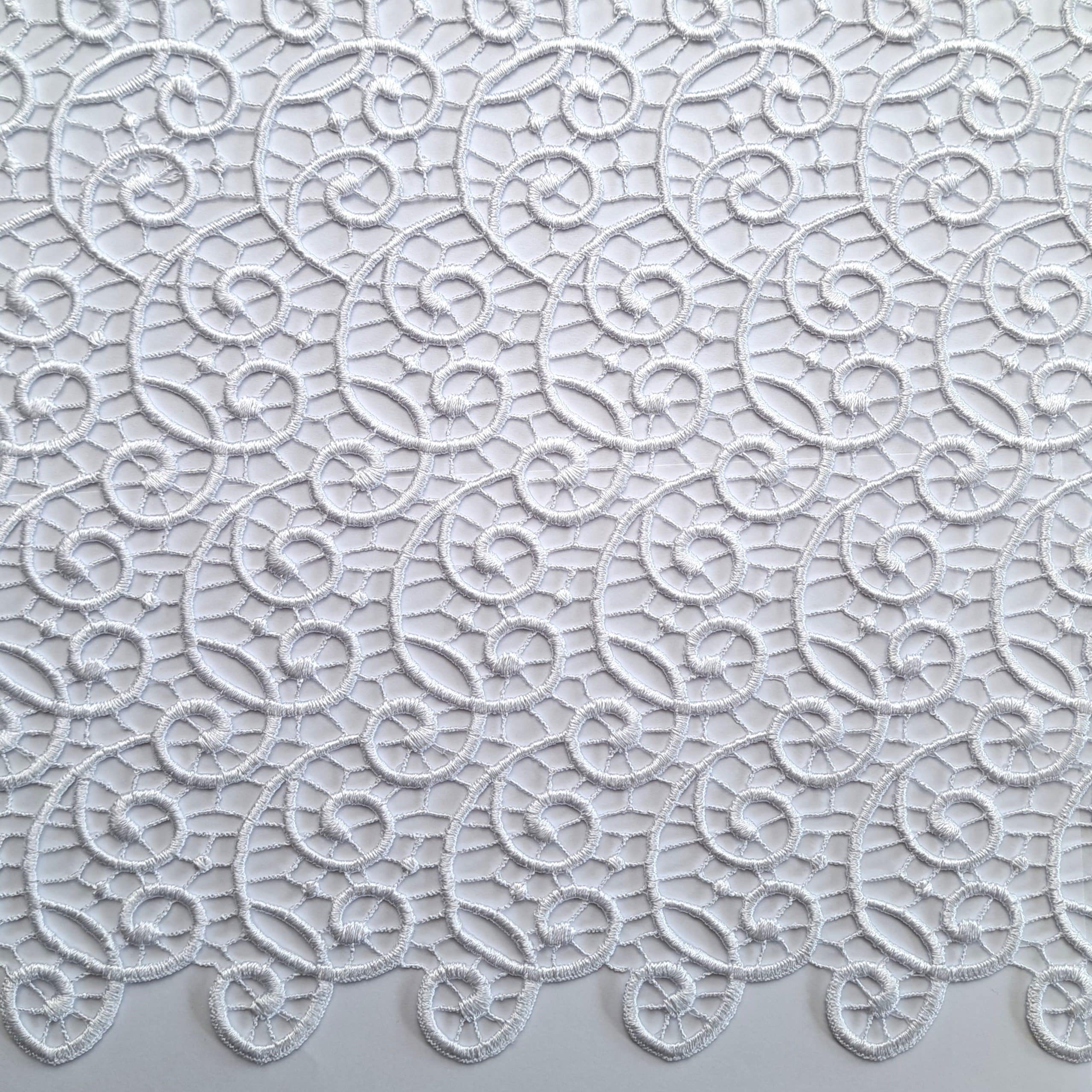 Białe koronkowe tło z finezyjnym wzorem spiralnym na przezroczystej tkaninie.