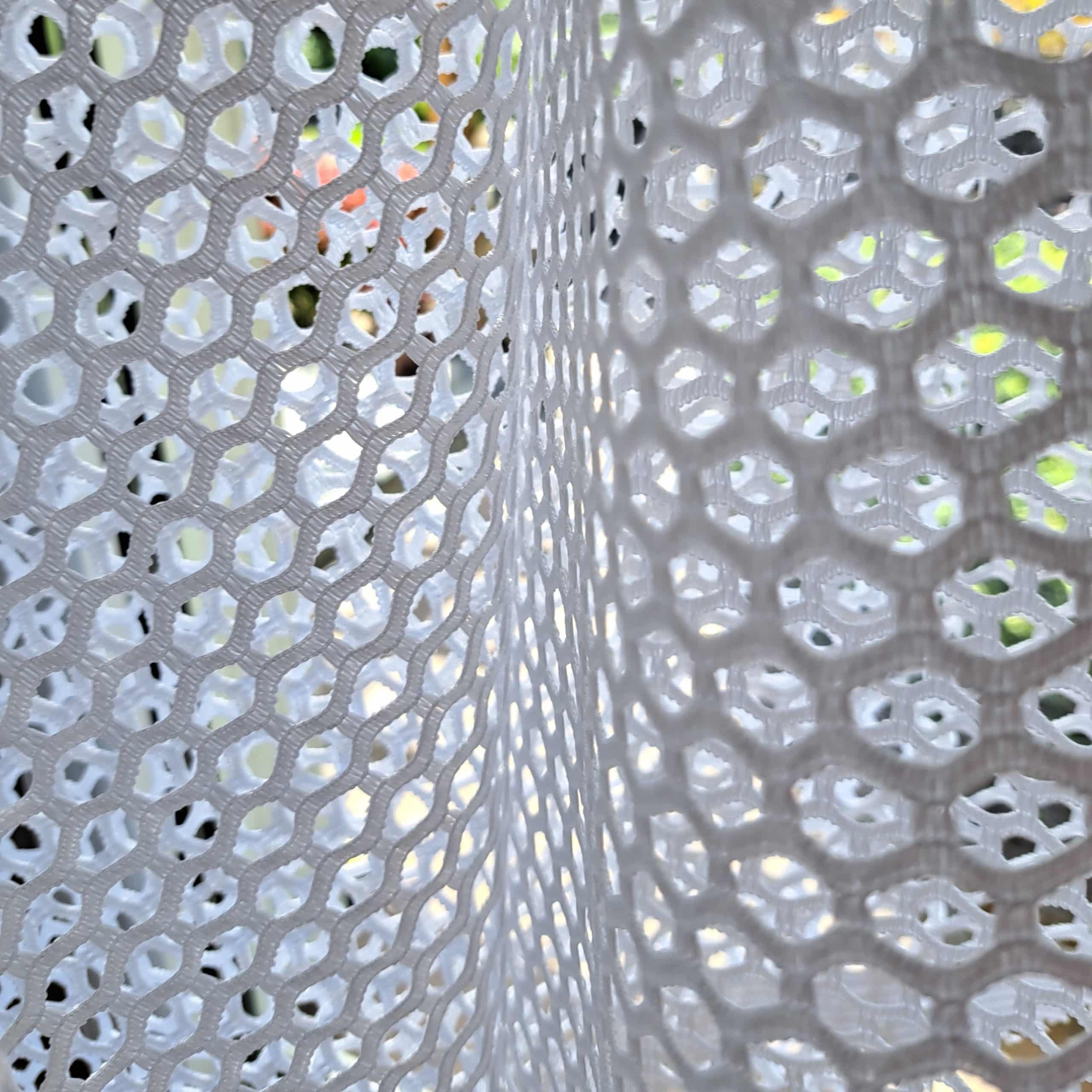 11607 bi 2 Biała siateczkowa zasłona z geometrycznym wzorem, światło przechodzi przez otwory.