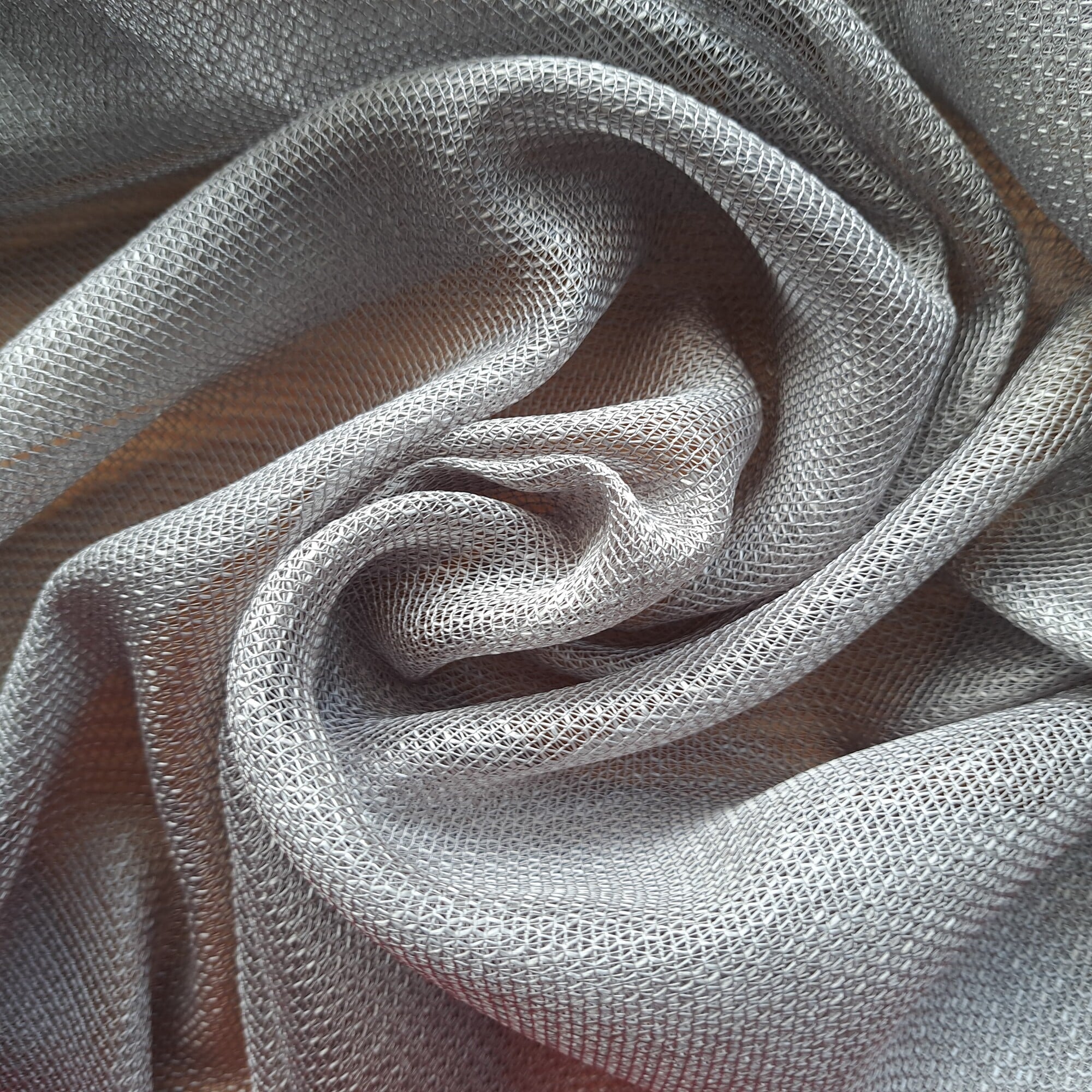 Szary materiał o fakturze siatkowej, złożony w falujące kształty. Subtelne zagniecenia, dekoracyjny tekstyl.