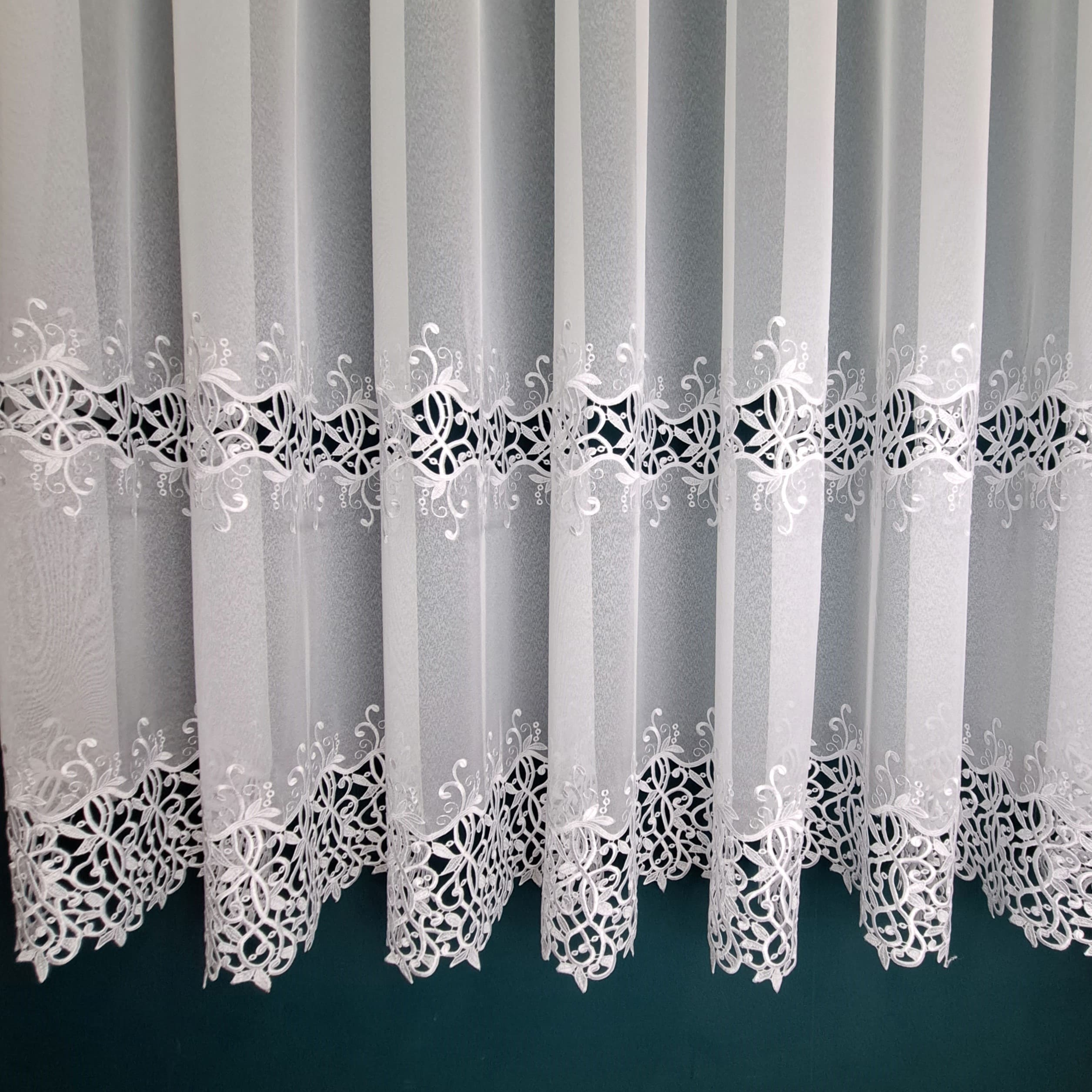 Firana haftowana biała 110 - 180 cm Długość 180cm  +/- 3% tolerancji. Firana z dwoma szlakami efektownego haftu. Wykonana na podkładzie klasycznej markizety. Szerokość dolnej aplikacji 20-25cm; górnej 18-22cm; odległość między szlakami ok. 23cm. Średni stopień przejrzystości. Miękka i przyjemna w dotyku. Tkanina cięta z belki, wymaga obszycia. Łatwa w utrzymaniu i konserwacji. Prać w temperaturze do 30 stopni. 100% poliester. Producent: Turcja Aplikacja chętnie kupowana przez naszych klientów. Zapraszamy :)