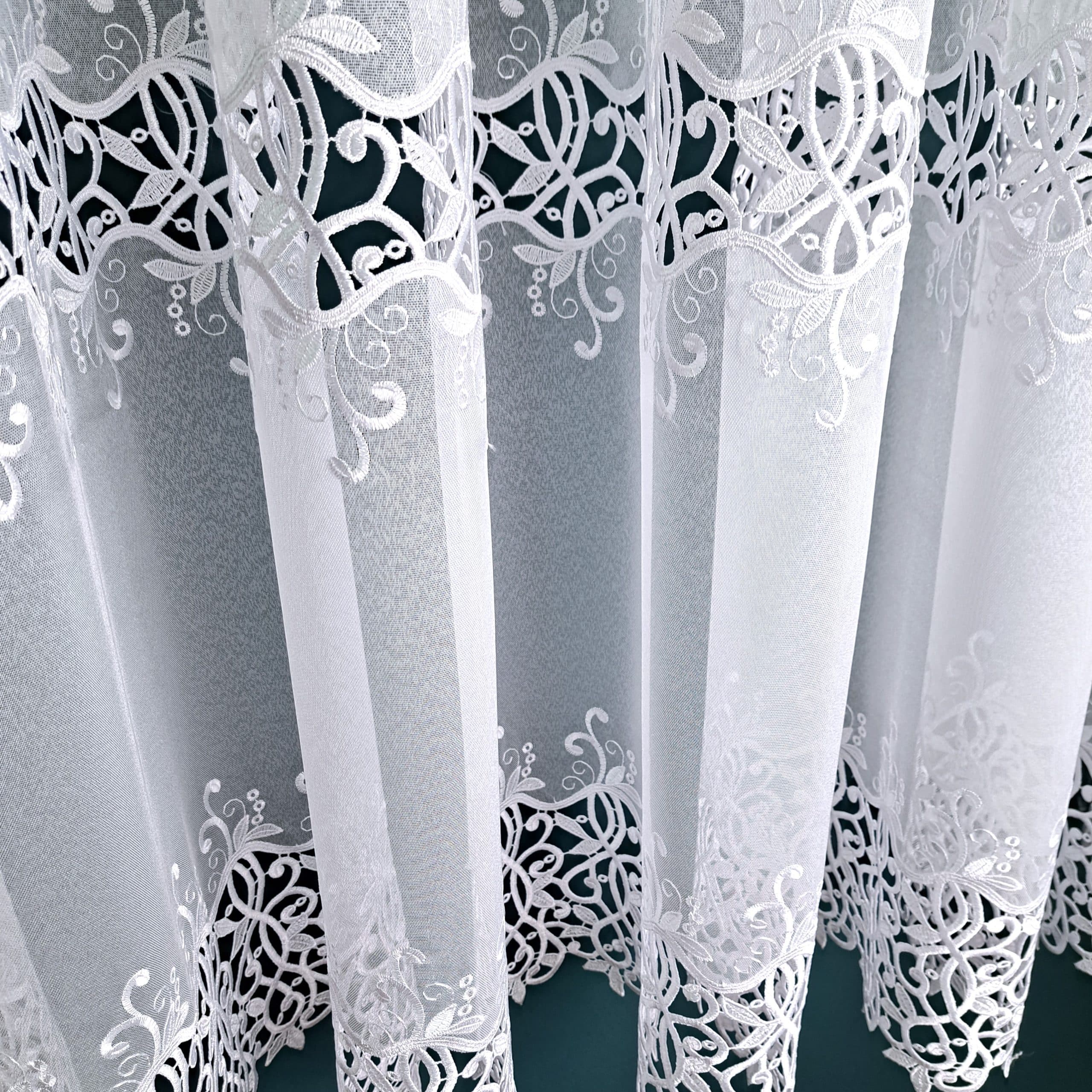 Białe zasłony z misternym, ozdobnym haftem na ciemnym tle, elegancka dekoracja wnętrza.