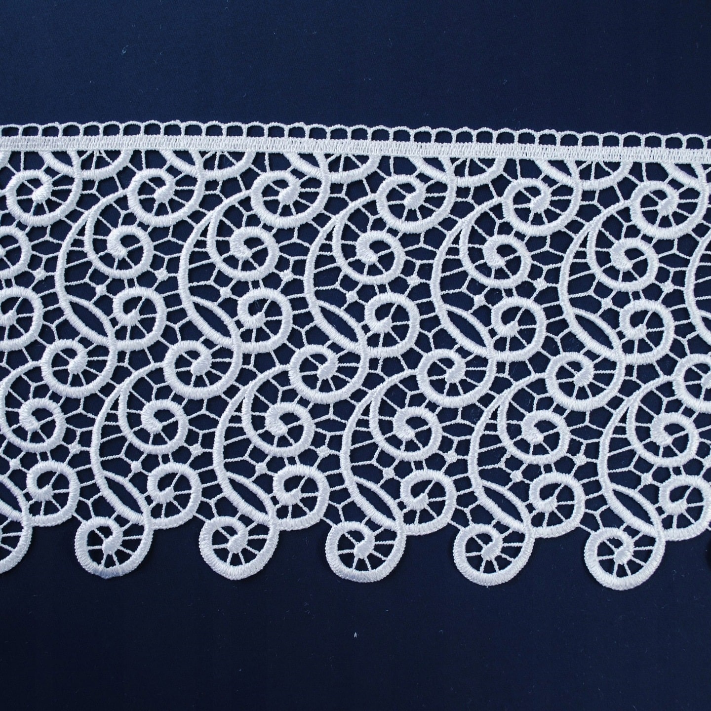 Koronkowy pas biegnący poziomo na ciemnym tle, ozdobiony białymi, skomplikowanymi wzorami.