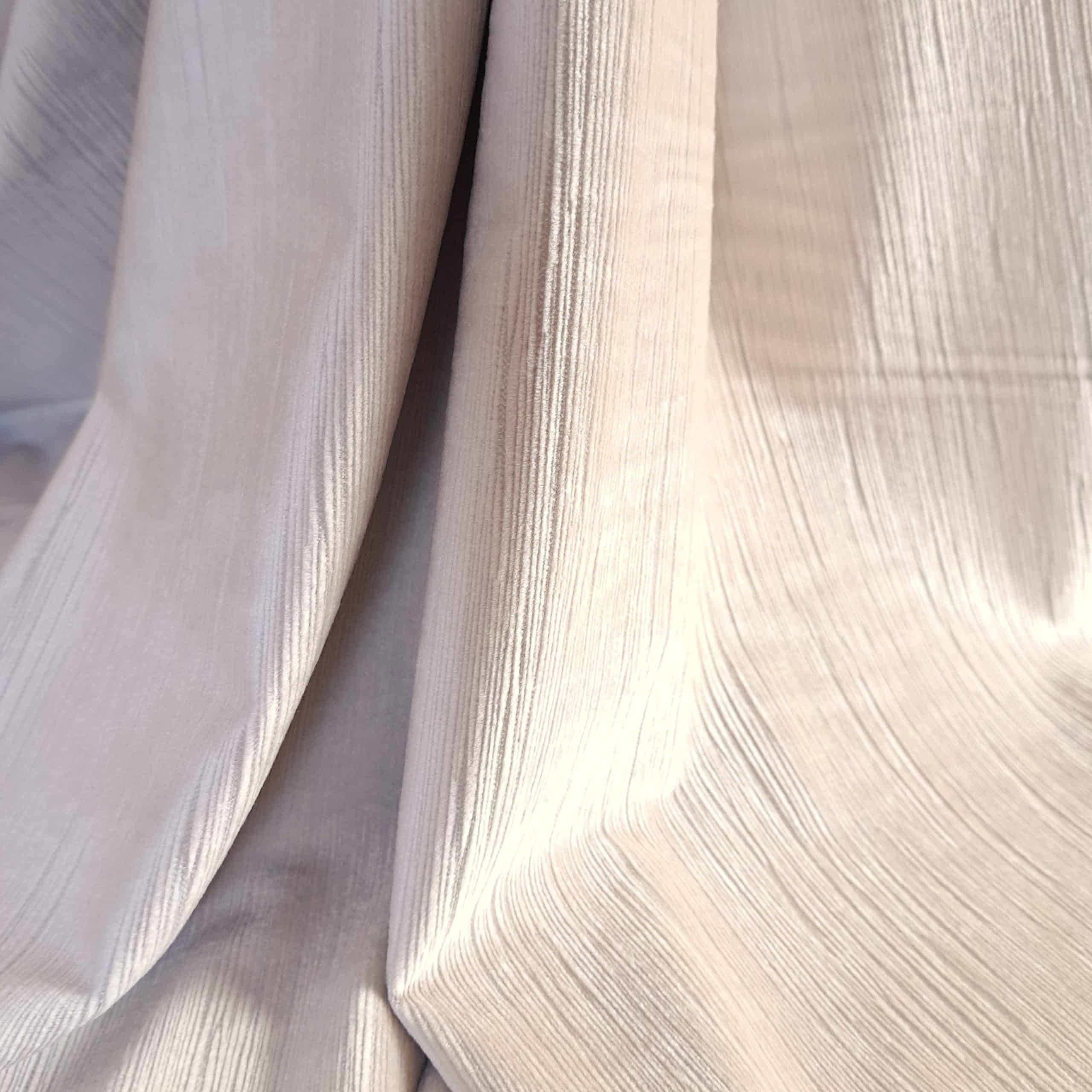 Beżowa, teksturowana tkanina z widocznymi pionowymi liniami, tworząca eleganckie fałdy.