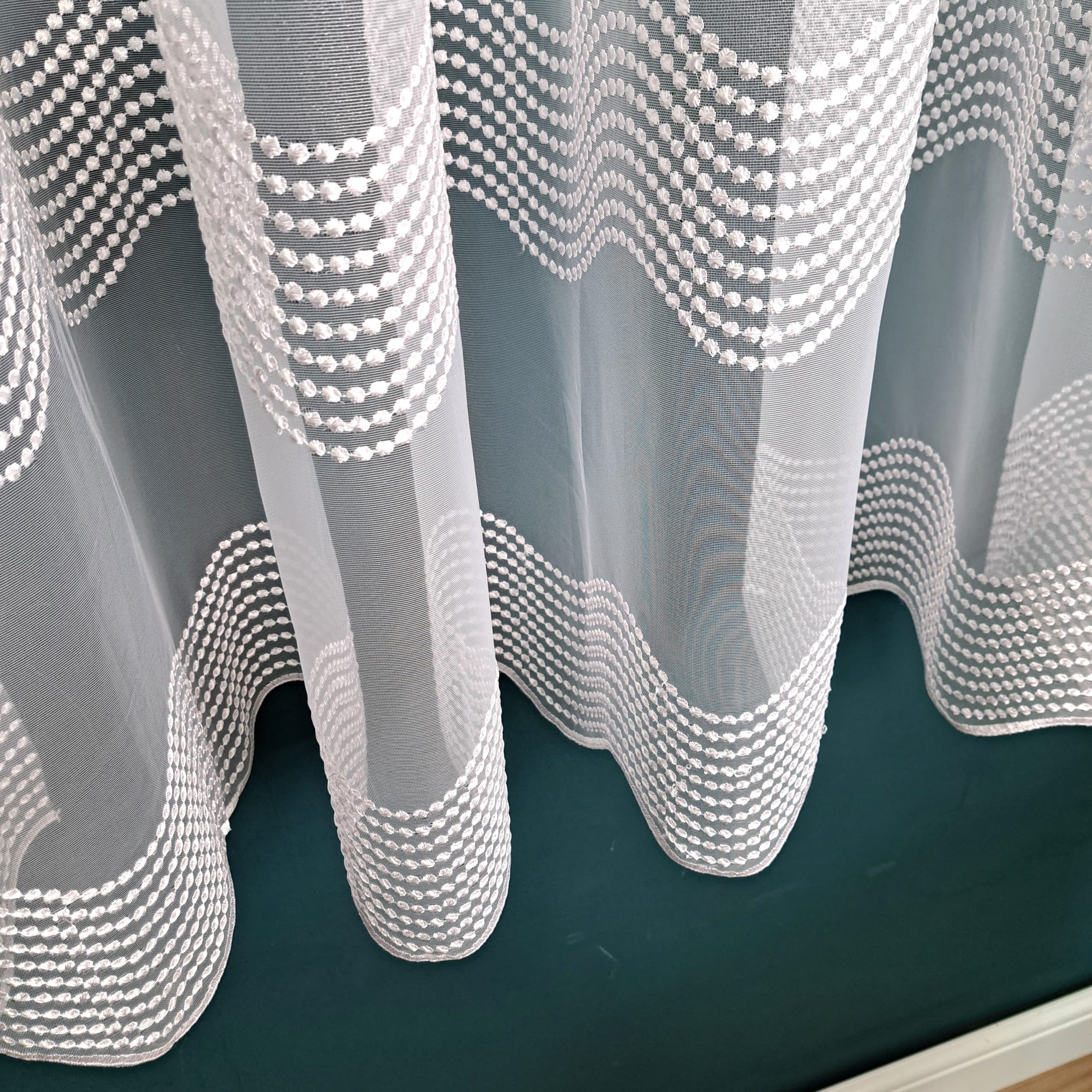 Biała firanka z haftem w faliste wzory na ciemnym tle, elegancka dekoracja okna.