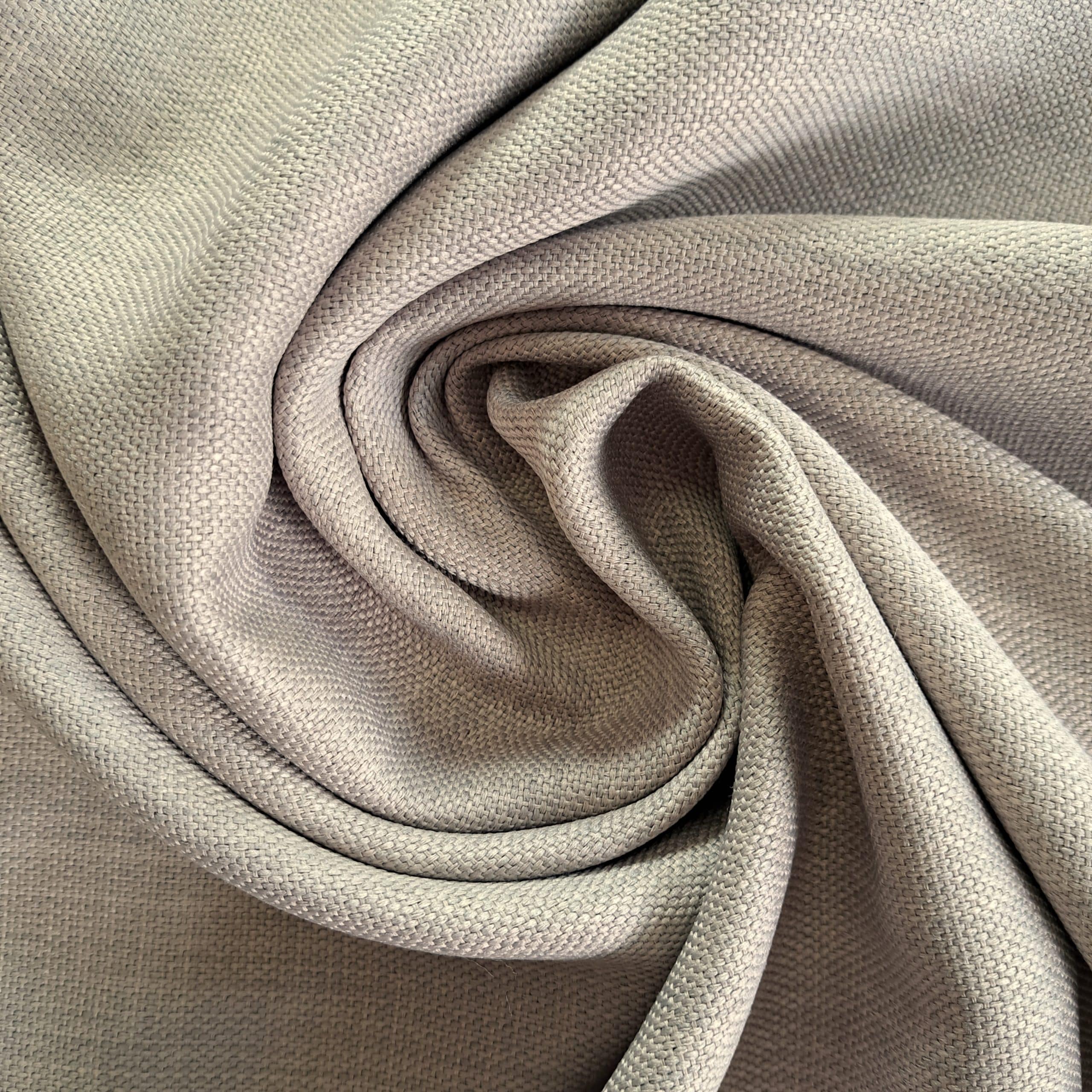 Beżowa tkanina z bliska, ułożona w spiralę, ukazująca strukturę materiału. Idealna na zasłony lub obicia.